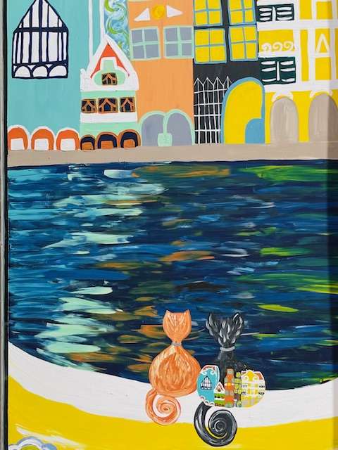 Colorful street art of two cats sittingon a wall overlooking water to the village opposite with multi-colored buildings in Curacao